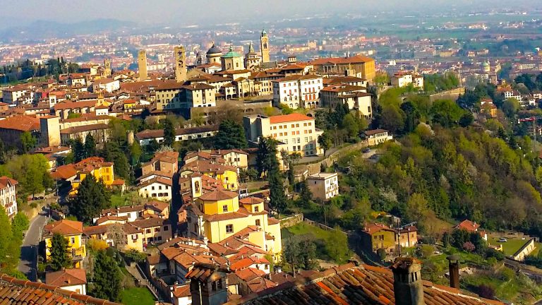 View of Bergamo from above, showing the old town rooftops, church towers, and surrounding hills