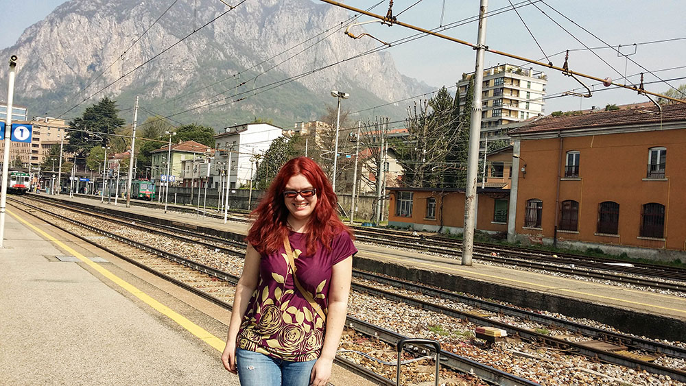 How to plan your first trip abroad 1 A woman standing on the platform at Lecco train station in Italy, with mountains in the background.