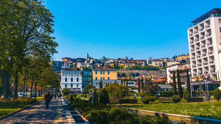View of Lower Bergamo with rooftops and streets, and the historic buildings of Upper Bergamo visible on the hill in the distance.