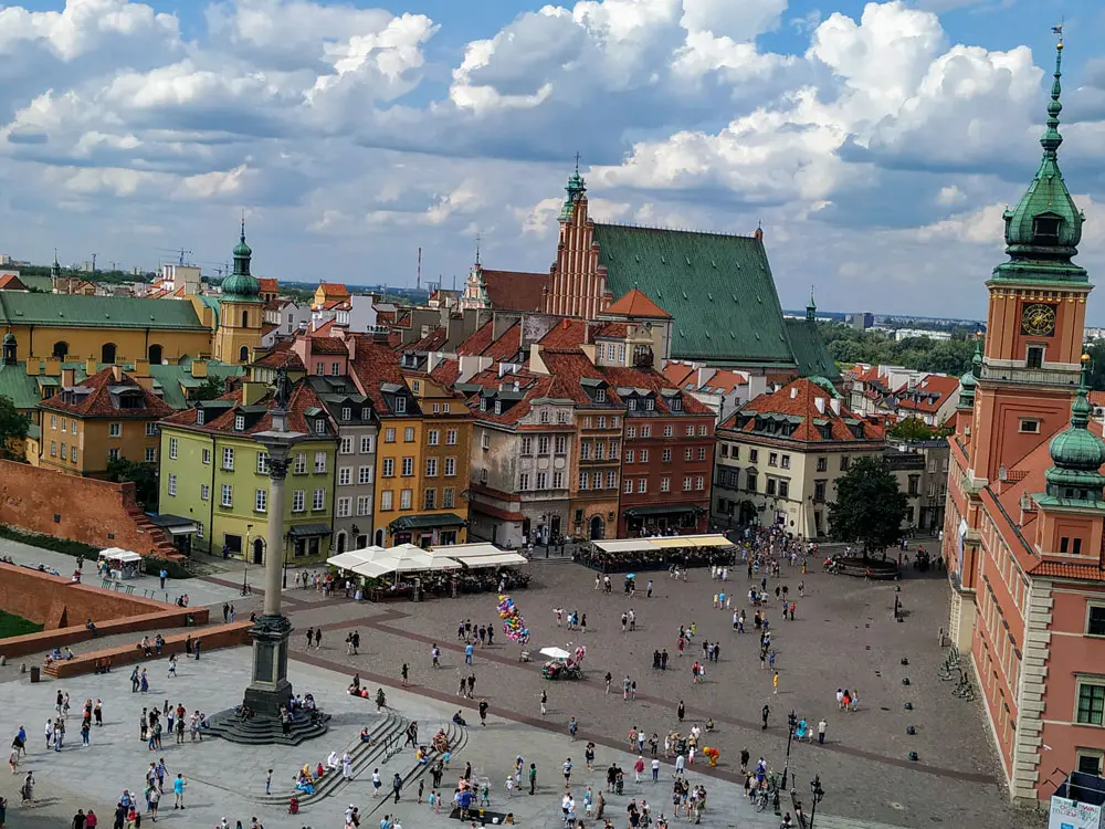 5 best cities in Europe for a first-time traveller 5 High-angle view of a square in Warsaw with a church tower, a monument, and people walking across the open space.