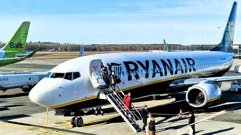 Travellers walking down the stairs from a Ryanair aircraft, with an airBaltic tail visible in the background.
