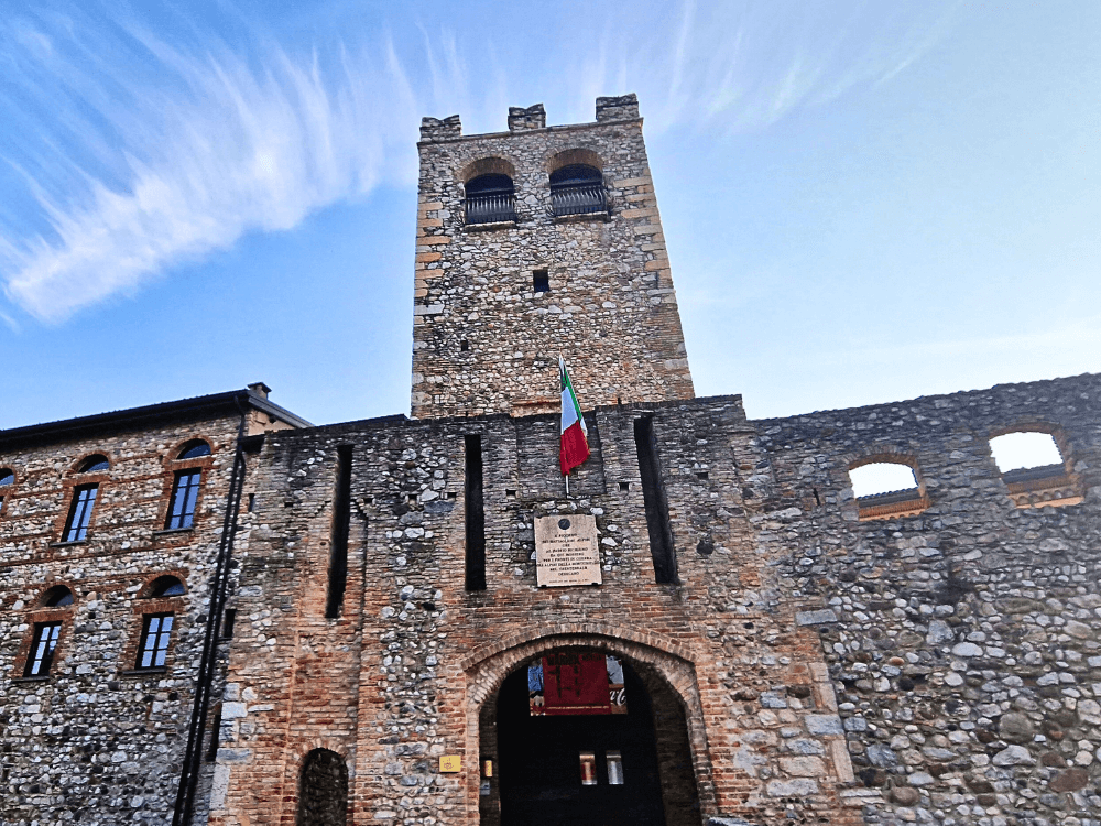 Where to stay on Lake Garda without a car: Peschiera or Desenzano? 6 View of Desenzano Castle taken while standing in front of the main gate, with the camera slightly lifted to show the arched entrance and the Italian flag above it.