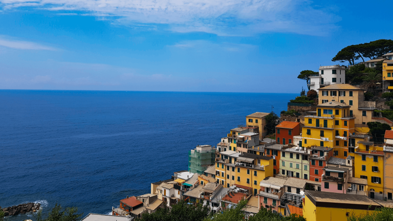 Riomaggiore in Cinque Terre seen from a higher viewpoint, with colourful houses stacked along the cliffs in late July.