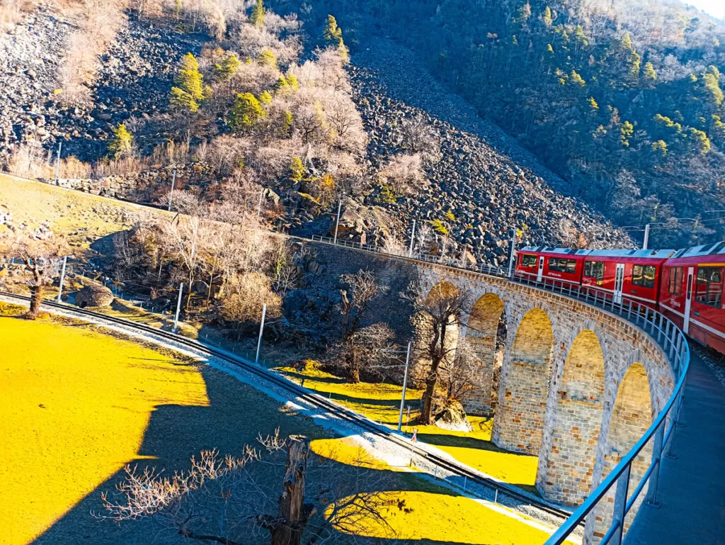 Bernina Express: a simple day trip into the Swiss Alps 5 A red Bernina Express train travelling across a stone viaduct in the mountains.