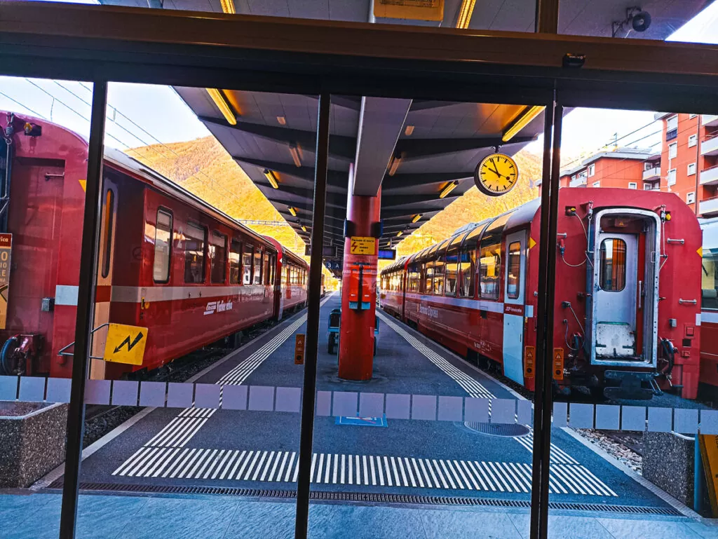 Bernina Express: a simple day trip into the Swiss Alps 3 Two red Bernina Express trains on the tracks, viewed through the glass doors of Tirano railway station.