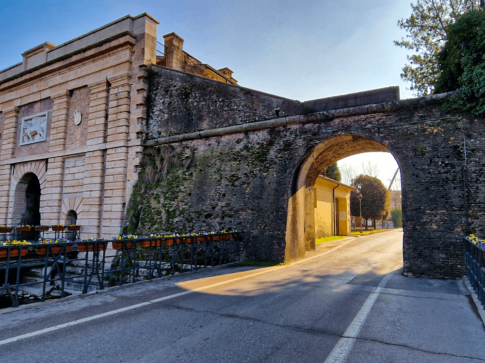 How to reach Lake Garda and its towns by public transport 1 A walkway from the train station leading over a bridge towards an arched gateway into the old town
