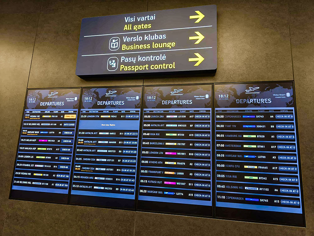 First time flying: what to do at the airport 5 Multiple departures screens list flights beneath a large direction sign. The sign reads Visi vartai All gates Verslo klubas Business lounge Pasu kontrole Passport control with arrows pointing right