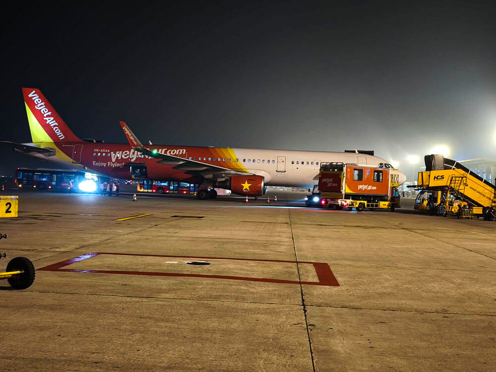 First time flying: what to do at the airport 11 A VietJet Air aircraft is parked on the apron at night under bright floodlights. Service vehicles and equipment stand alongside the plane near the wing and fuselage.