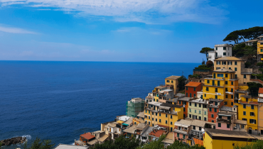 Riomaggiore in Cinque Terre seen from a higher viewpoint, with colourful houses stacked along the cliffs in late July.