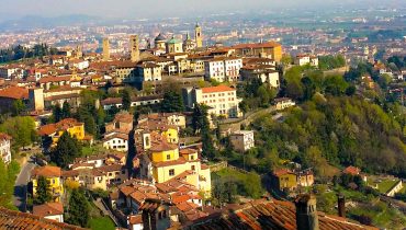 View of Bergamo from above, showing the old town rooftops, church towers, and surrounding hills