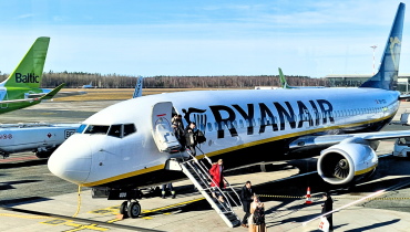Travellers walking down the stairs from a Ryanair aircraft, with an airBaltic tail visible in the background.